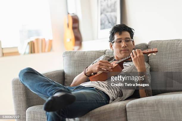usa, new jersey, jersey city, man sitting on sofa and playing ukulele - ukulele stock-fotos und bilder
