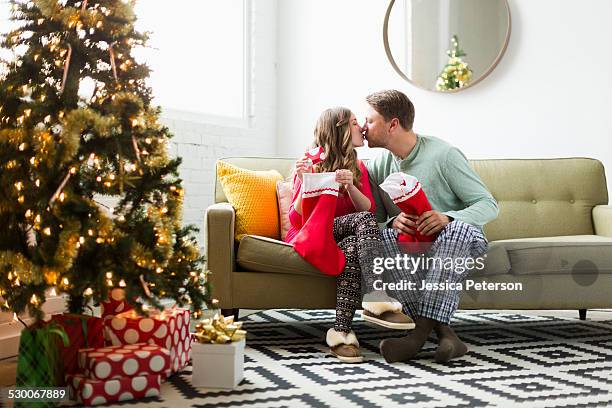 young couple with christmas stockings kissing on sofa - calza della befana foto e immagini stock