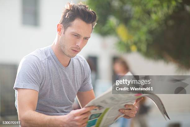 portrait of young man reading newspaper - junger mann liest zeitung stock-fotos und bilder