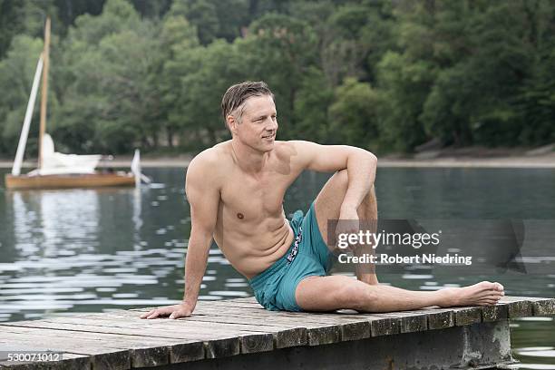 mature man sitting on wooden pier and smiling, bavaria, germany - zwembroek stockfoto's en -beelden