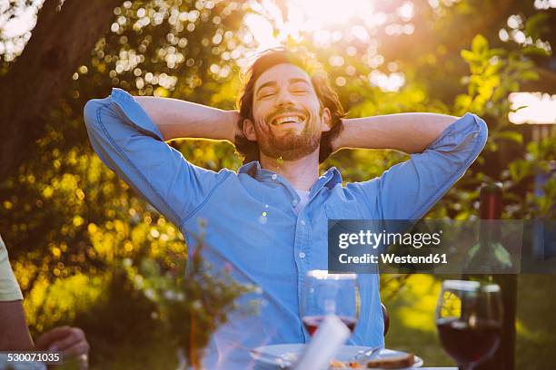 man leaning back and smiling at dinner in evening light - evening indulgence stock pictures, royalty-free photos & images