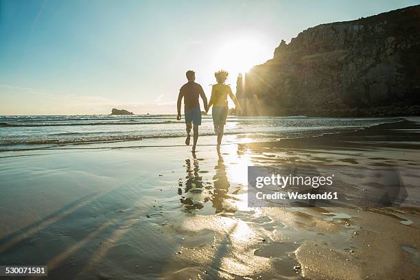 france, brittany, camaret-sur-mer, teenage couple running on the beach - boy and girl running along beach holding hands stock-fotos und bilder