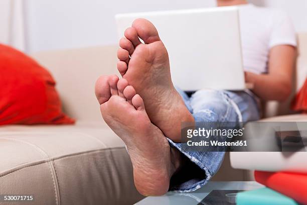 man sitting barefoot on a couch using laptop at home - male feet soles 個照片及圖片檔