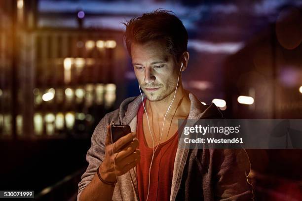 portrait of young man with smartphone and earphones listening music at night - munich night stock pictures, royalty-free photos & images