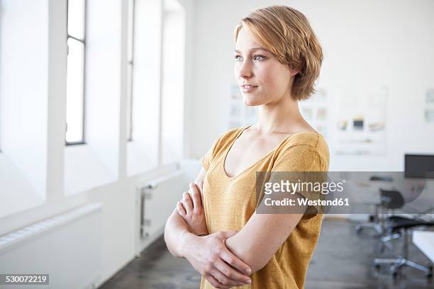 portrait of young woman with crossed arms in a creative office - seitenansicht stock-fotos und bilder