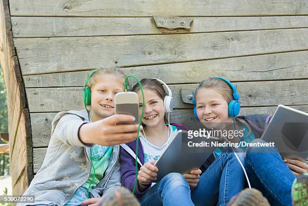 three friends sitting in playground and listening music, munich, bavaria, germany - film interactive music day 3 stock-fotos und bilder
