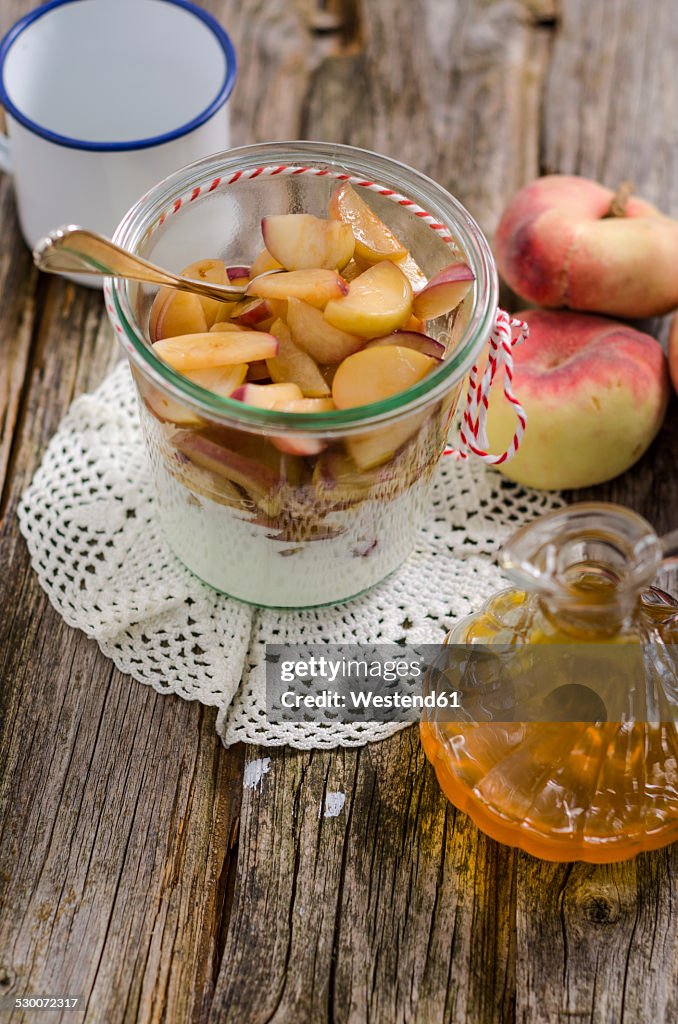 Glass of peaches on natural yoghurt and carafe of peach sirup