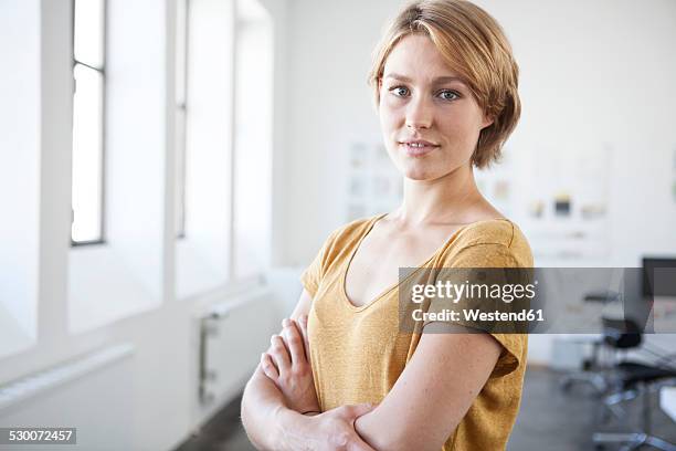 portrait of young woman with crossed arms in a creative office - young blonde woman facing away photos et images de collection