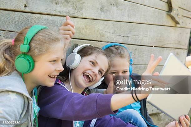 three friends sitting in playground and listening music, munich, bavaria, germany - bavaria girl stockfoto's en -beelden