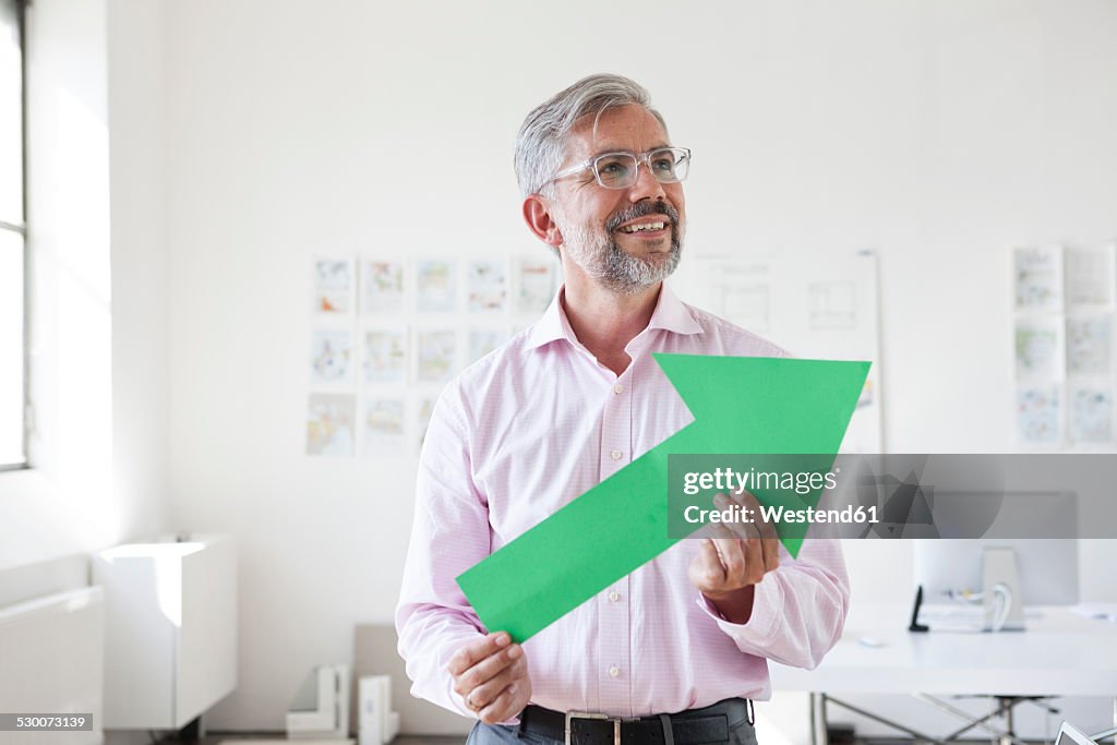 Portrait of smiling businessman holding green arrow