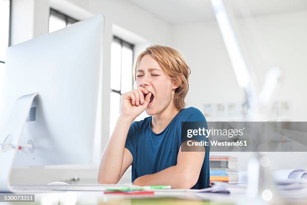 portrait of yawning young woman at her desk in a creative office - yawn office stock pictures, royalty-free photos & images