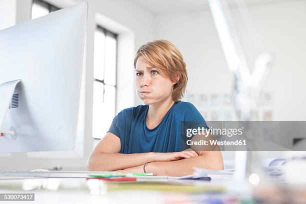 portrait of young woman pouting a mouth at her desk in a creative office - grimacing 個照片及圖片檔