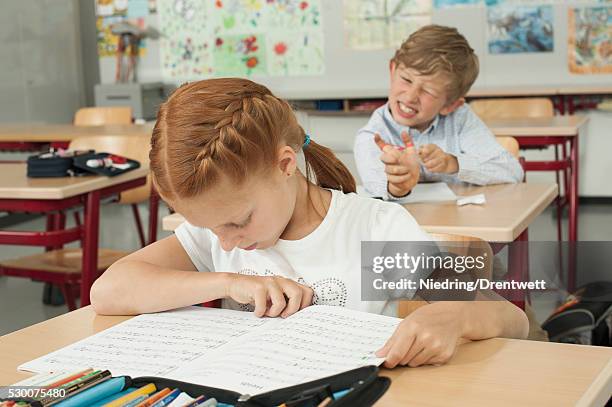 schoolboy disturbing a schoolgirl with slingshot in classroom, munich, bavaria, germany - taquiner photos et images de collection