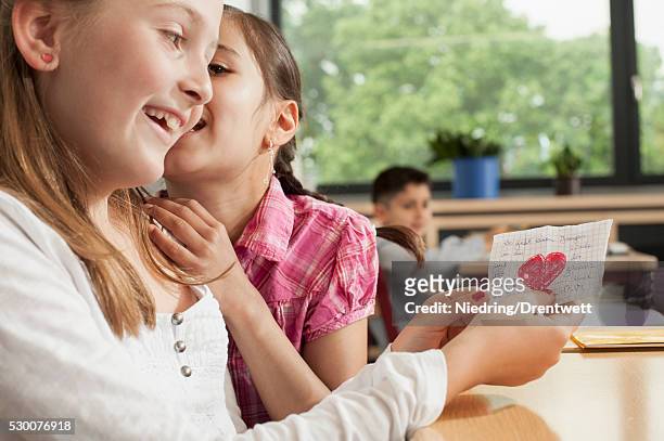 schoolgirls whispering in classroom and showing a love letter, munich, bavaria, germany - love letter stock-fotos und bilder