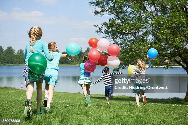 rear view of girls running in park with balloons, lake karlsfeld, munich, bavaria, germany - children only braided ponytail stock pictures, royalty-free photos & images