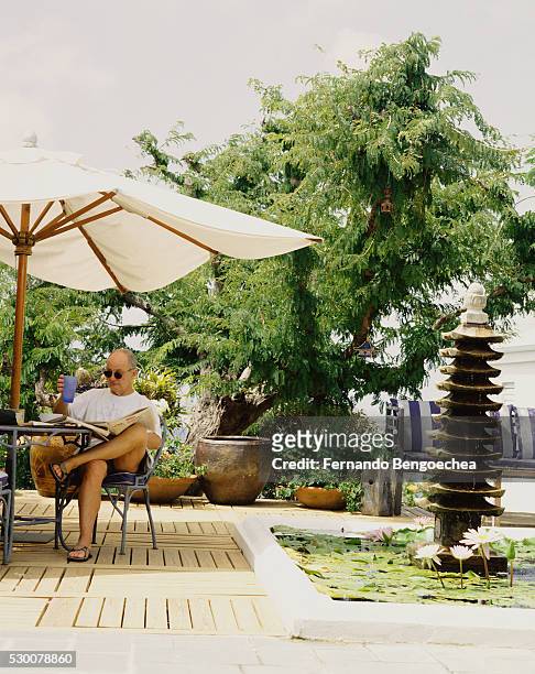douglas cramer reading newspaper on patio - garden umbrella stock pictures, royalty-free photos & images