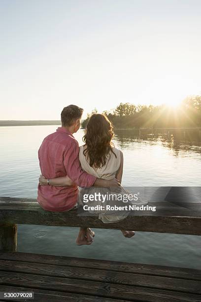 mature couple sitting on pier looking at sunset, bavaria, germany - long jetty stock pictures, royalty-free photos & images