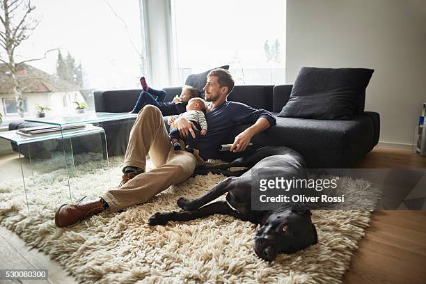father with dog and two children relaxing in living room - family dog stock-fotos und bilder
