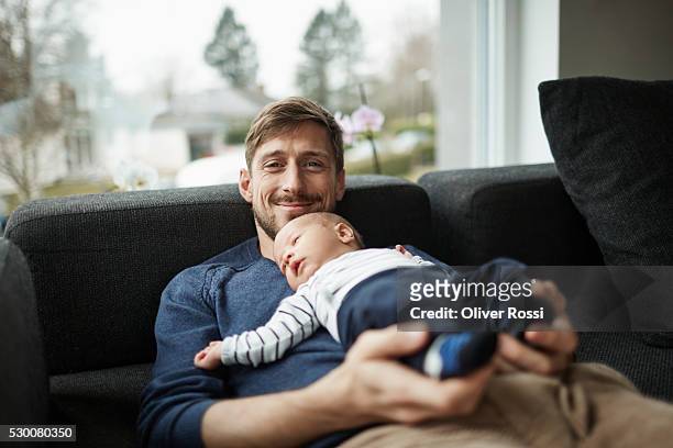 smiling father and baby boy lying on couch - father baby stock pictures, royalty-free photos & images