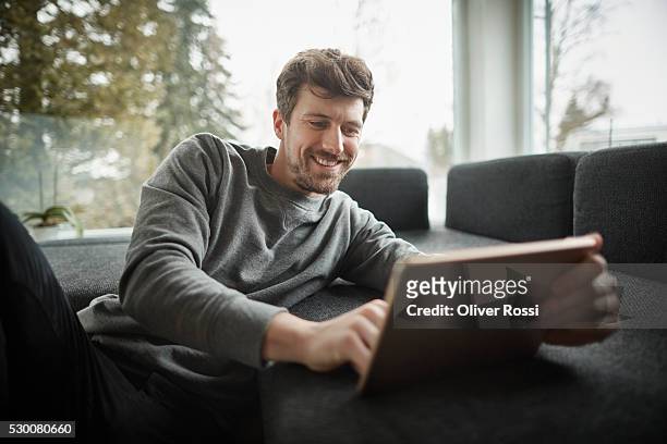 smiling man using digital tablet on couch - homme ipad photos et images de collection