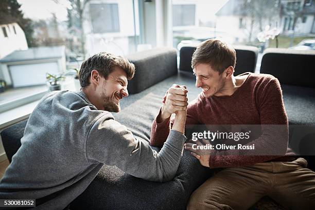 two friends arm wrestling living room - arm wrestle stock pictures, royalty-free photos & images