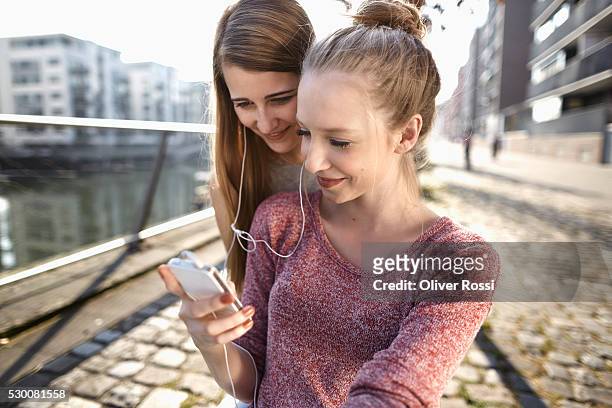 two friends sharing earbuds from smartphone - sharing headphones stock pictures, royalty-free photos & images