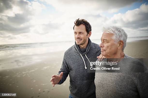 senior man with adult son on the beach - hand on shoulder stock pictures, royalty-free photos & images