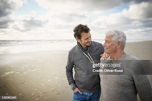 senior man with adult son on the beach - son stock pictures, royalty-free photos & images
