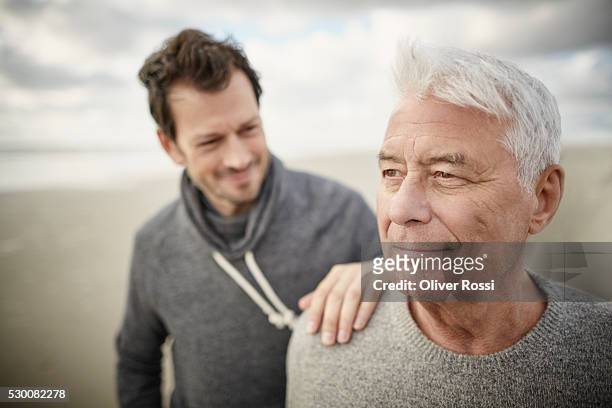 senior man with adult son on the beach - senior adult stock-fotos und bilder