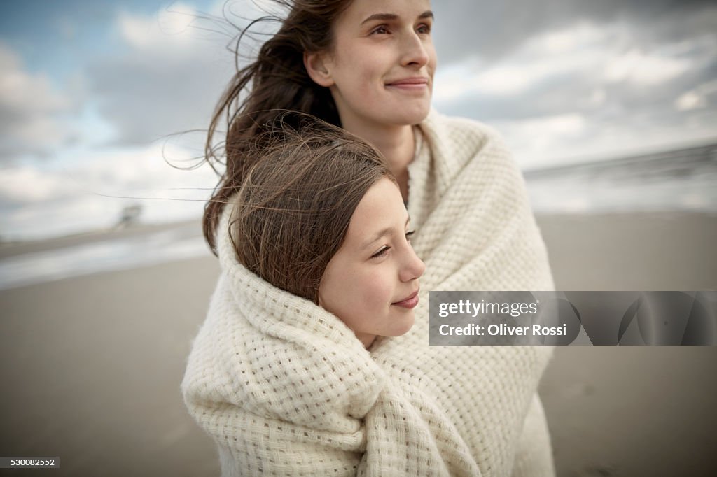 Mother and daughter wrapped in a shawl on the beach