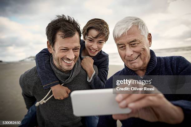 grandfather, father and son with cell phone on the beach - grandpa son stock pictures, royalty-free photos & images