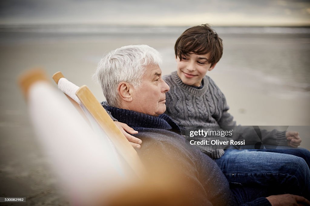 Grandfather and grandson on the beach relaxing in deckchair