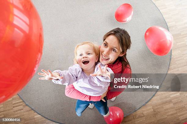 female educator and little girl playing with red balloons in kindergarten - rood kleed stockfoto's en -beelden