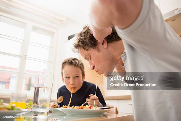 father and son eating spaghetti in kitchen - the joys of eating spaghetti stock pictures, royalty-free photos & images