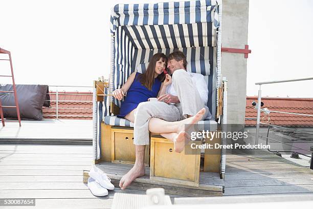 couple eating strawberry in roofed wicker beach chair, smiling - beach shelter stock-fotos und bilder