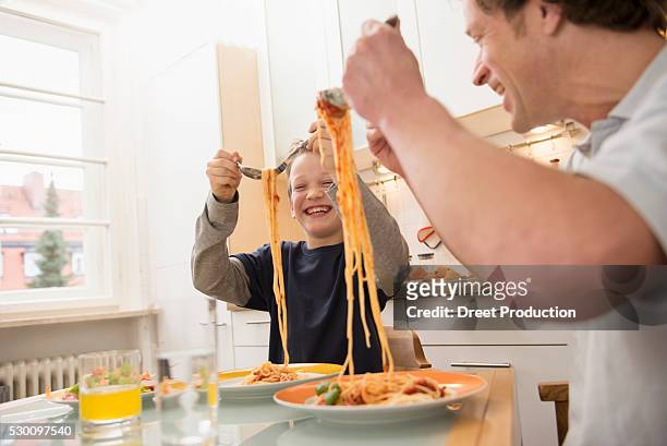 father and son eating spaghetti in kitchen - the joys of eating spaghetti stock pictures, royalty-free photos & images