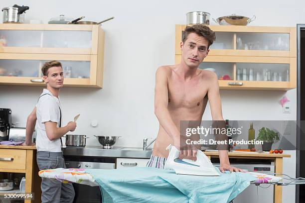 man ironing clothes while another man cooking in background - iron wine stock pictures, royalty-free photos & images