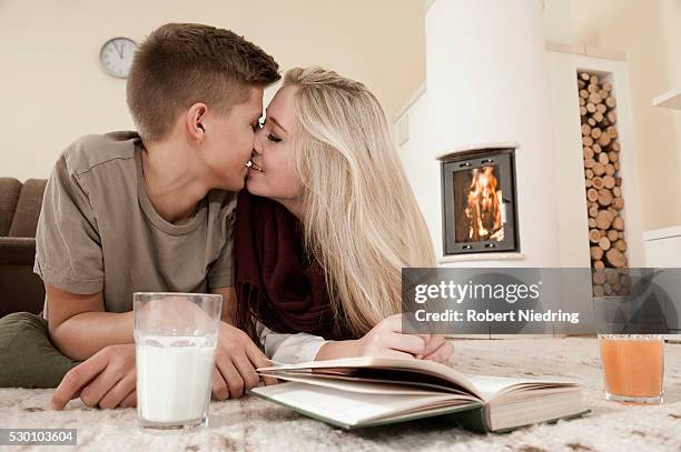 teenage couple in love cuddling on carpet in front of fireside - haardvuur stockfoto's en -beelden