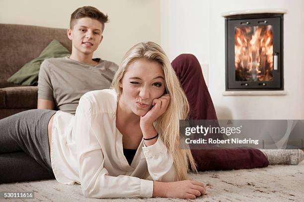teenage couple relaxing on carpet in front of fireside - tiener koppel stockfoto's en -beelden