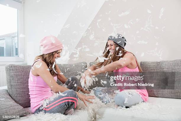 two female friends sitting on couch at home having pillow fight - pillow fight stock pictures, royalty-free photos & images