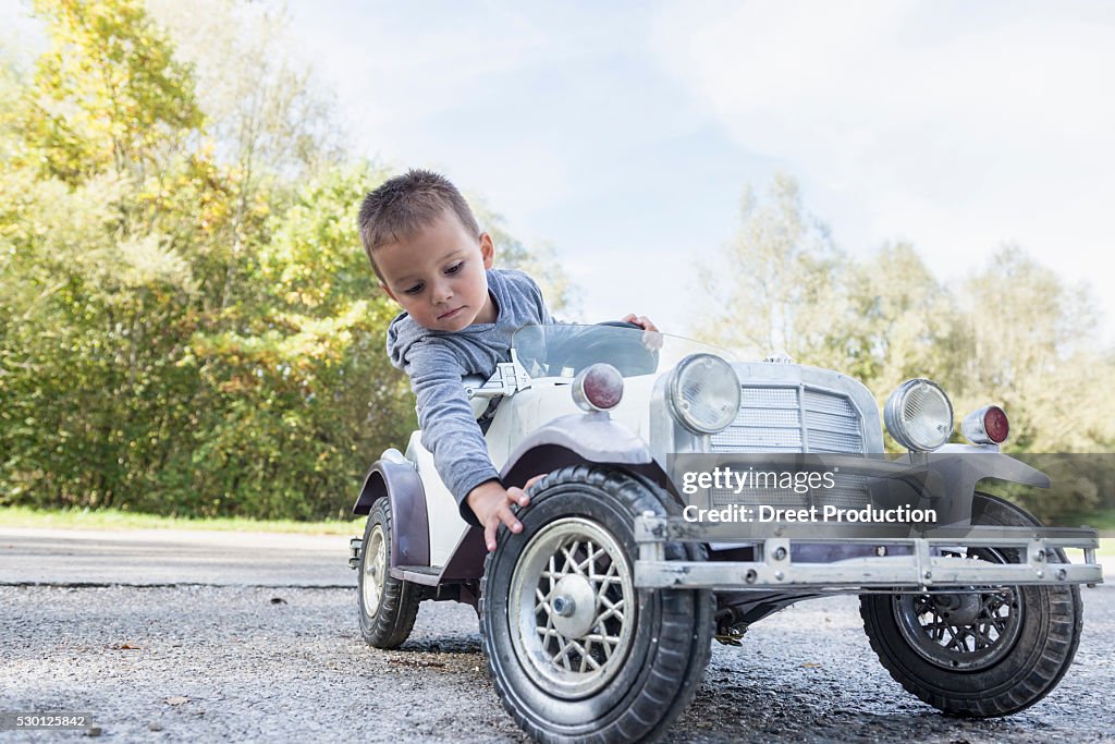 Portrait small boy checking tire model vintage car
