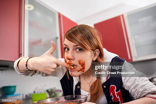 young woman eating tomato sauce in kitchen, munich, bavaria, germany - finger in mouth stockfoto's en -beelden