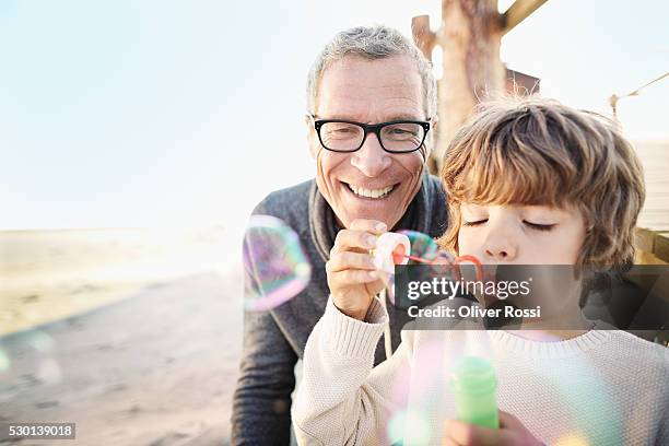 happy grandfather and grandson blowing soap bubbles on the beach - grandfather foto e immagini stock