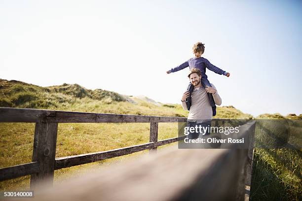 father carrying son on shoulders at the coast - huckepack nehmen stock-fotos und bilder
