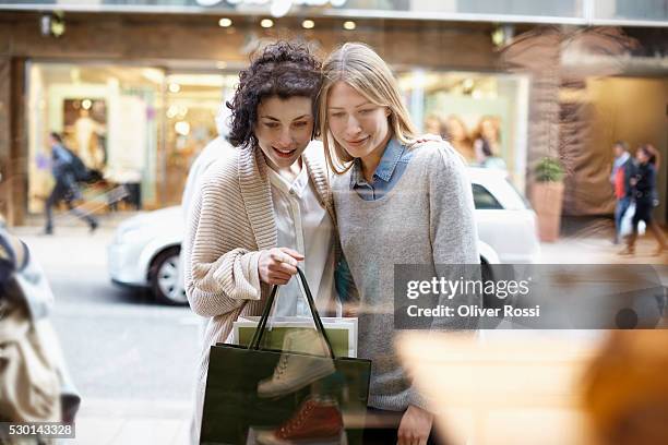 two young women looking in shop window - window shopping stock-fotos und bilder