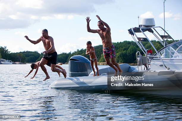 fathers with sons jumping into sea from motorboat - kinder badeboot stock-fotos und bilder