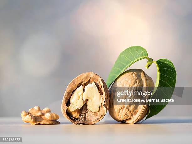 whole and broken walnuts on a wooden table illuminated by sunlight - walnuts stockfoto's en -beelden