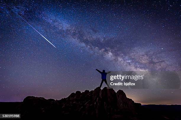 man with bright shooting star under milky way galaxy - light pollution stock pictures, royalty-free photos & images