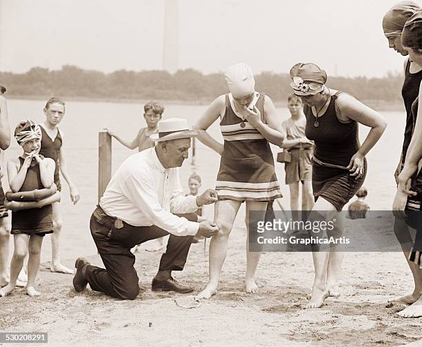 Woman having her swimsuit measured for length violations on a Washington DC beach in the 1920s , 1922.