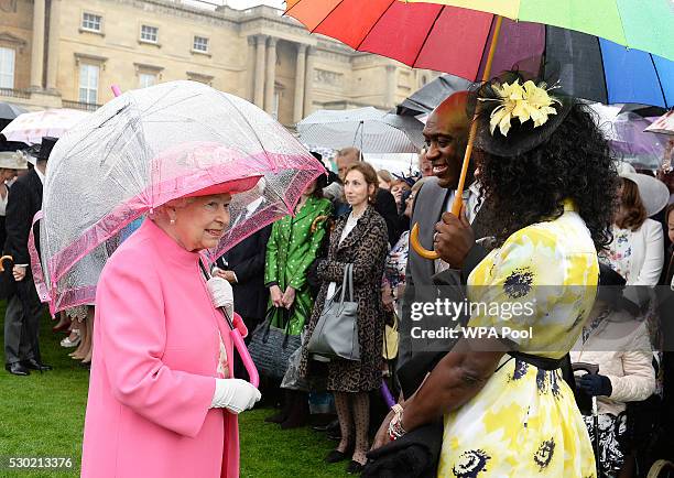 Queen Elizabeth II shelters from the rain under an umbrella as she talks to guests during the first Royal Garden Party of the year in the grounds of...